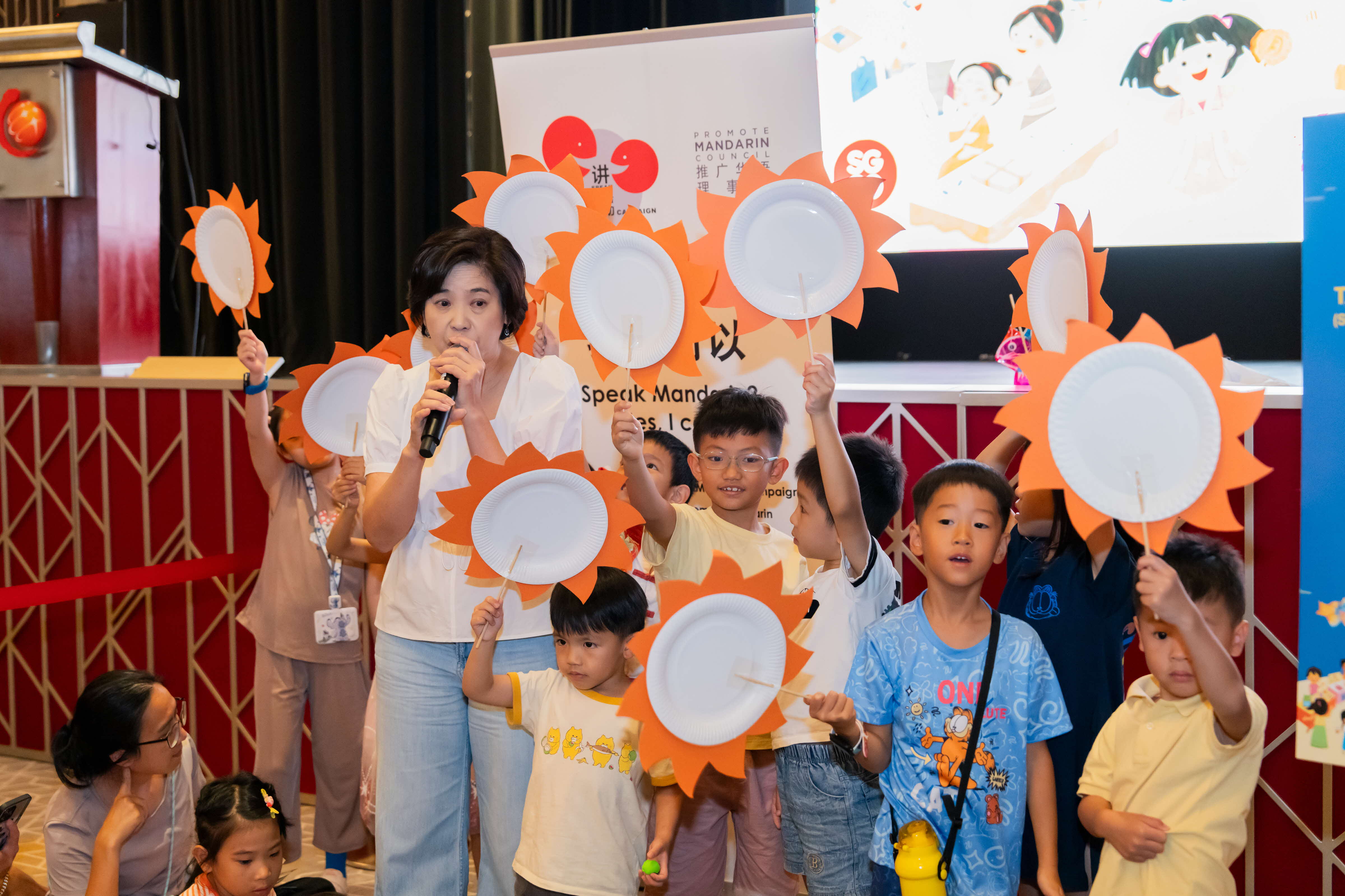 storyteller surrounded by children holding up crafts resembling the sun